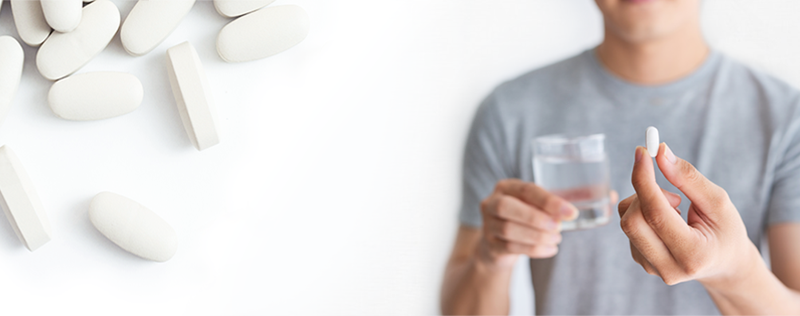 close up of man holding pill and glass of water
